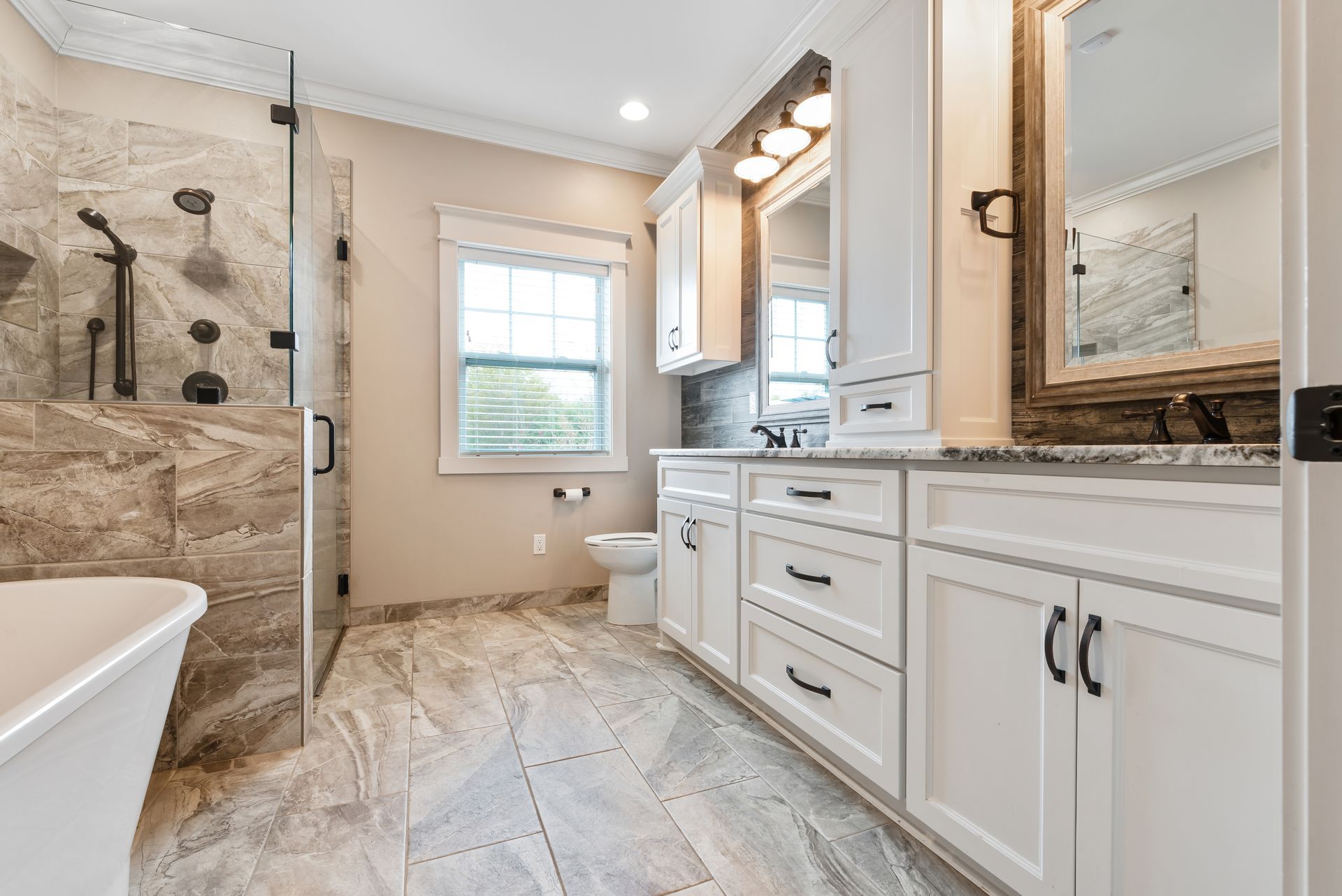 Bright, modern bathroom with white cabinets, stone tile, and a glass shower.