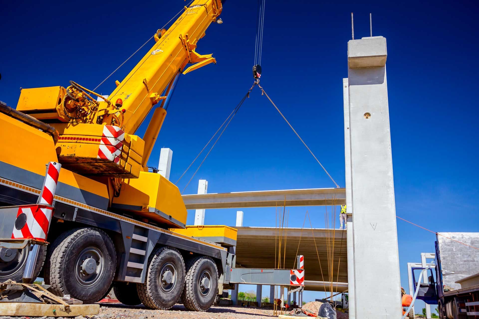 Yellow crane lifting a concrete beam at a construction site on a sunny day.