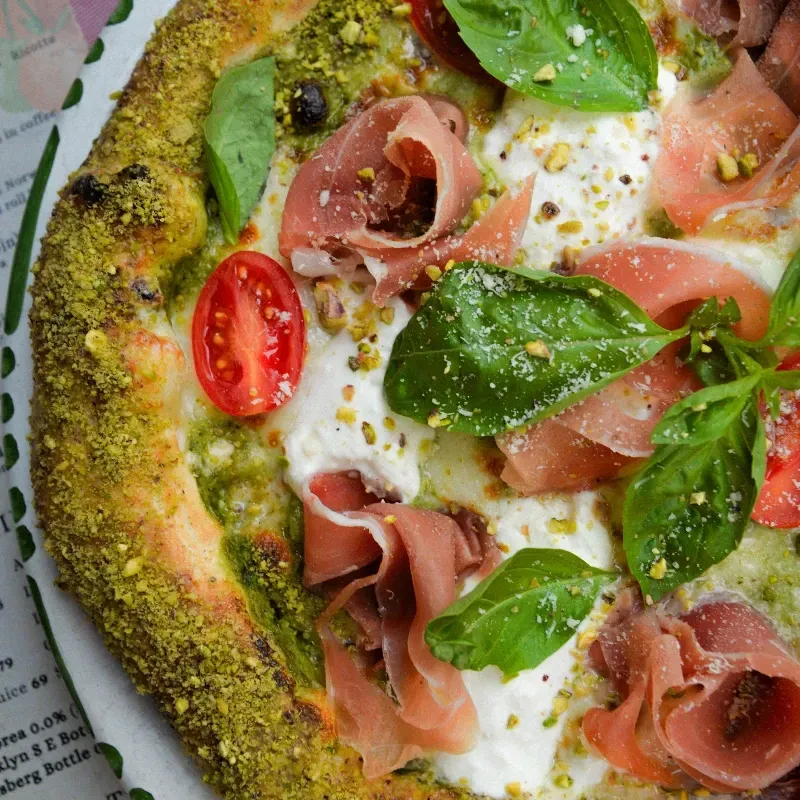 Pizza with spiral of white sauce, ground meat, basil, and charred crust, on a blue plate.