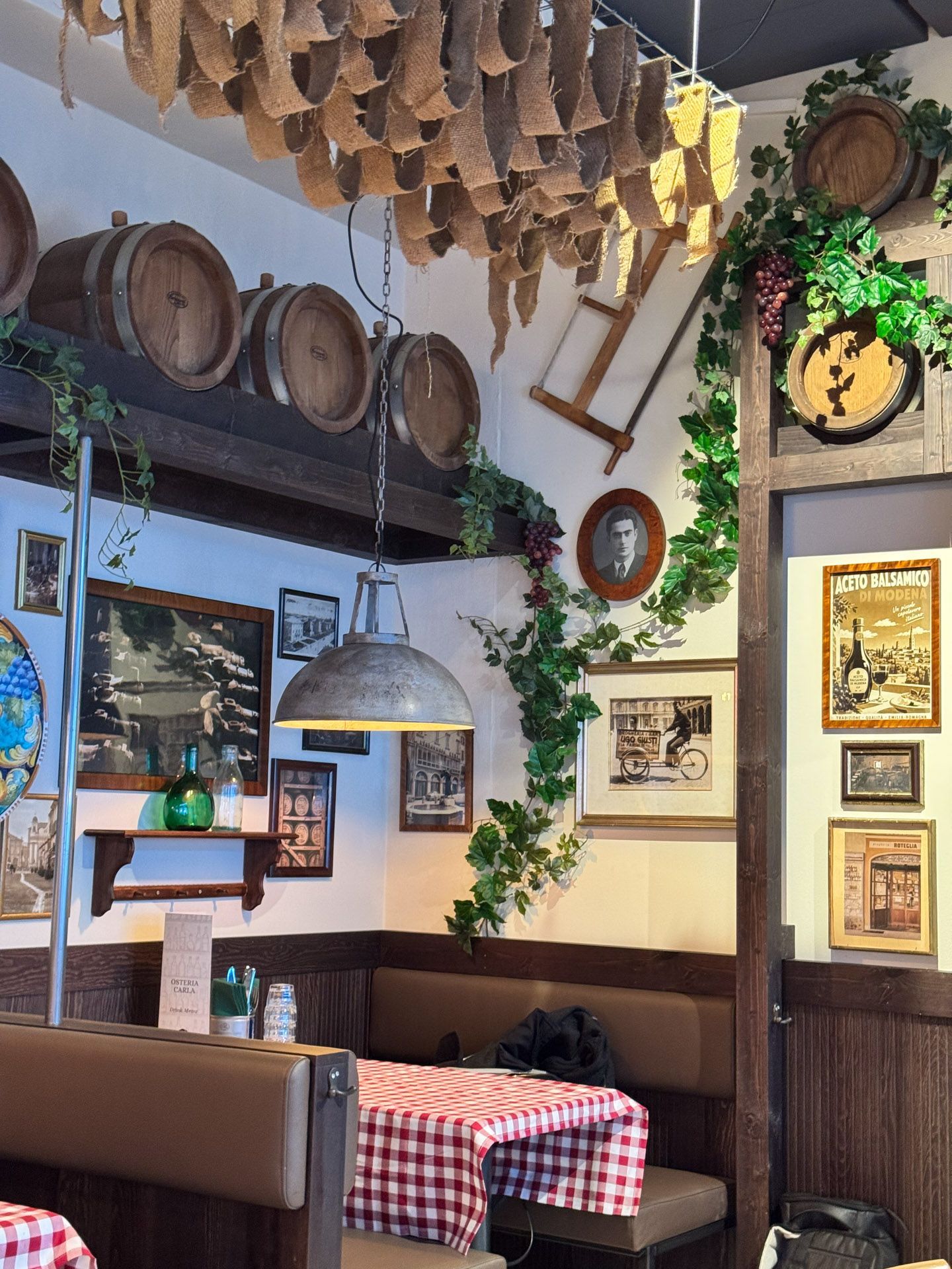 Cozy restaurant interior with patrons at checkered tablecloth tables under string lights and a neon sign.