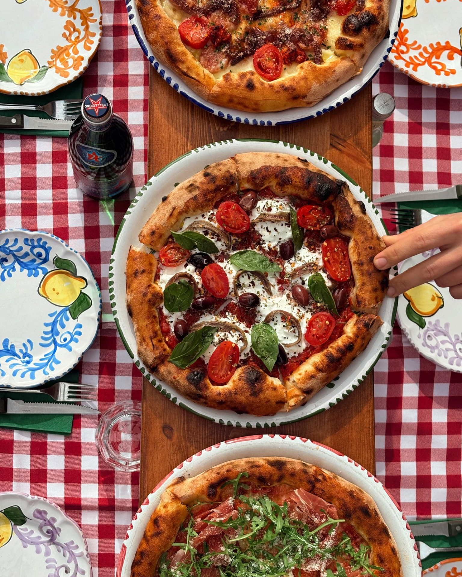 Pizza with toppings, pasta, and a drink on a checkered table.