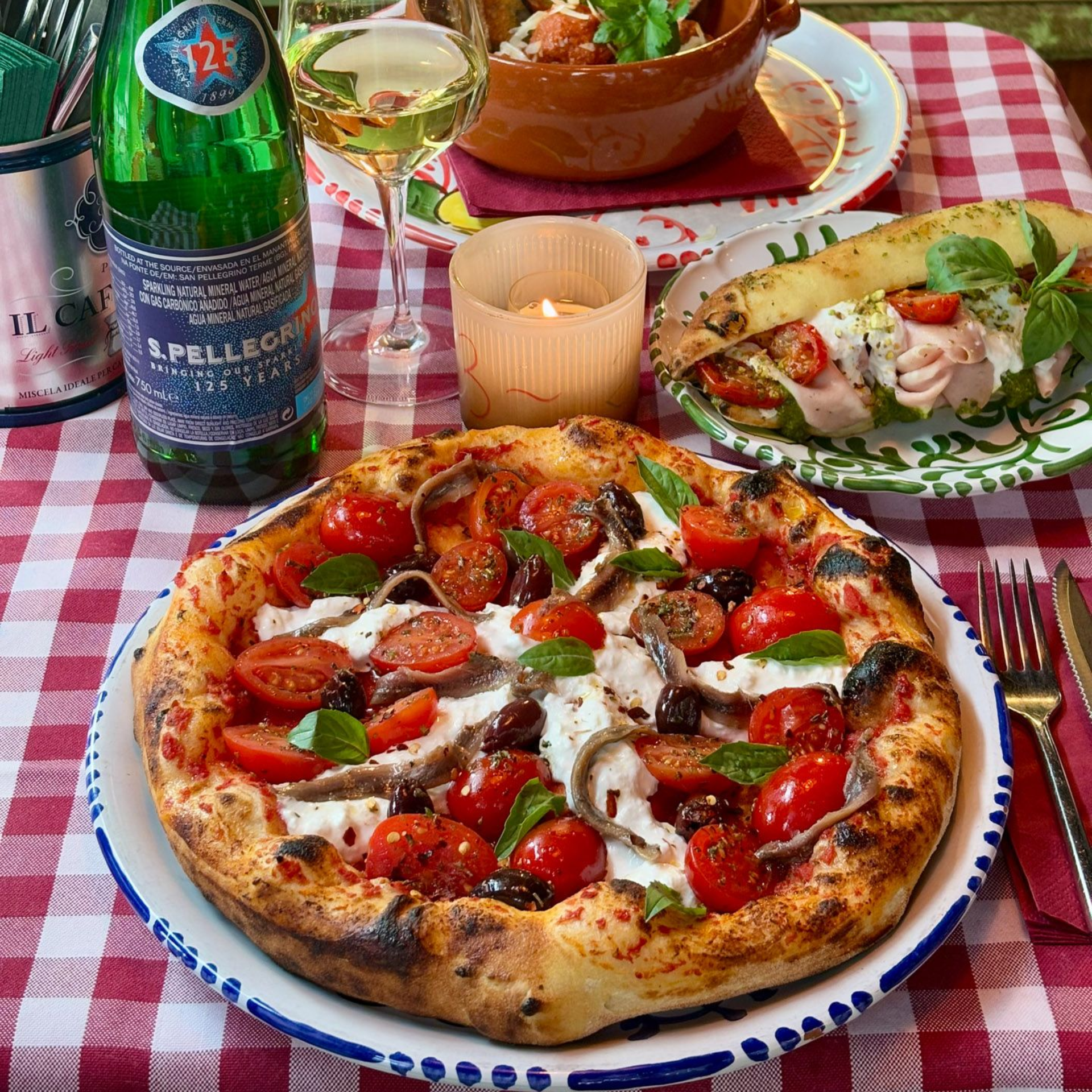 Pizza with toppings, pasta, and a drink on a checkered table.