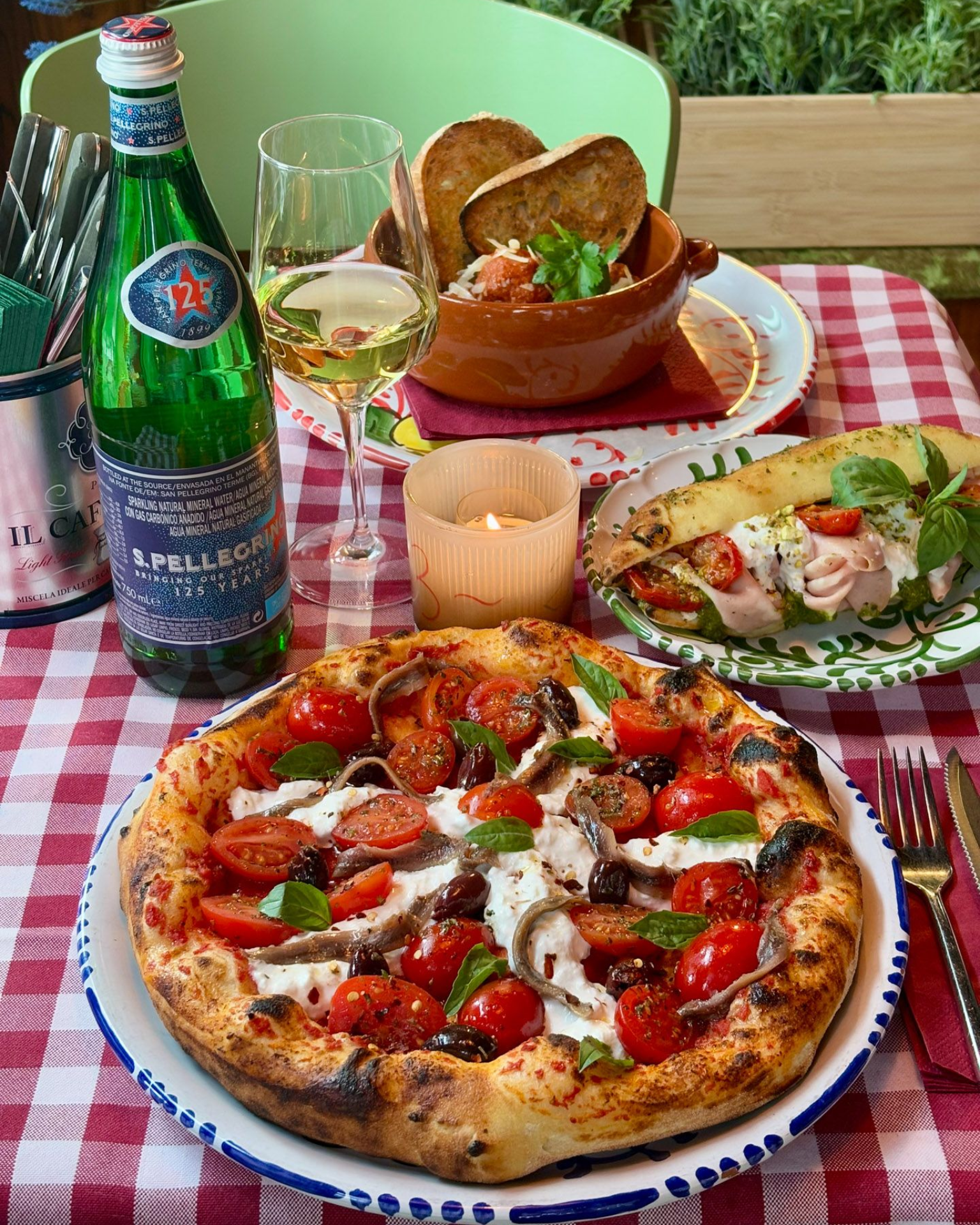 Pizza with toppings, pasta, and a drink on a checkered table.