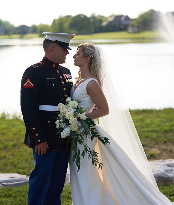 A bride and groom standing next to each other in front of a lake