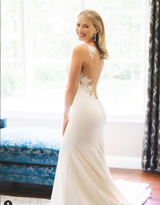 A woman in a white wedding dress is standing in front of a window.
