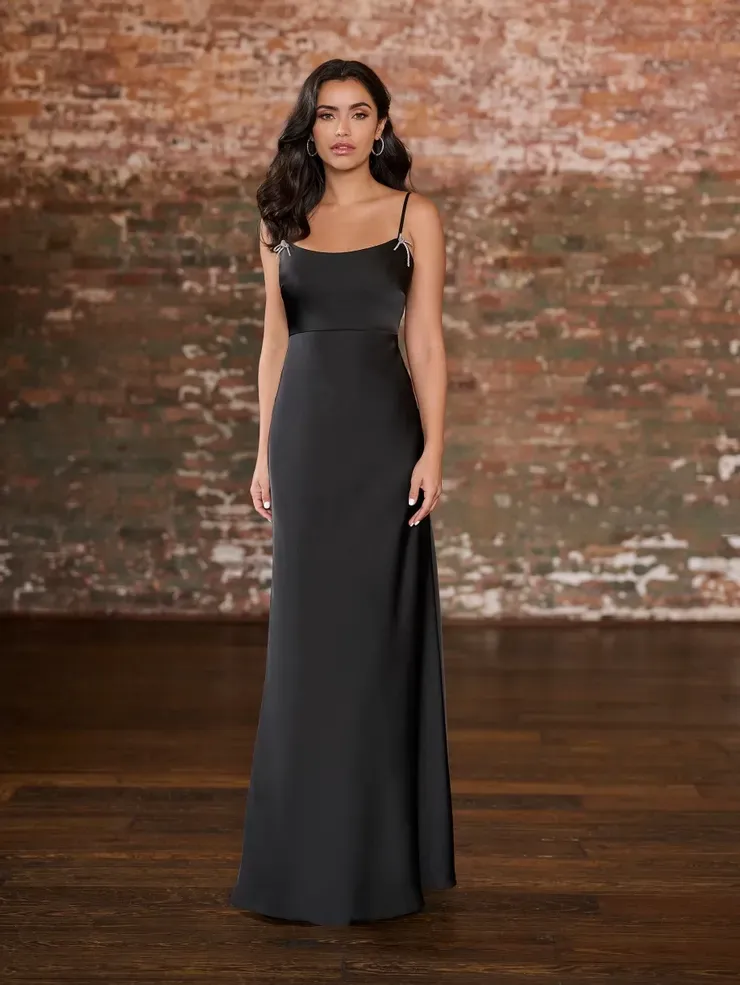 A woman in a black dress is standing in front of a brick wall.