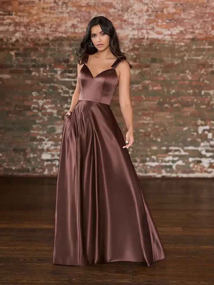 A woman is wearing a long brown satin dress in front of a brick wall.
