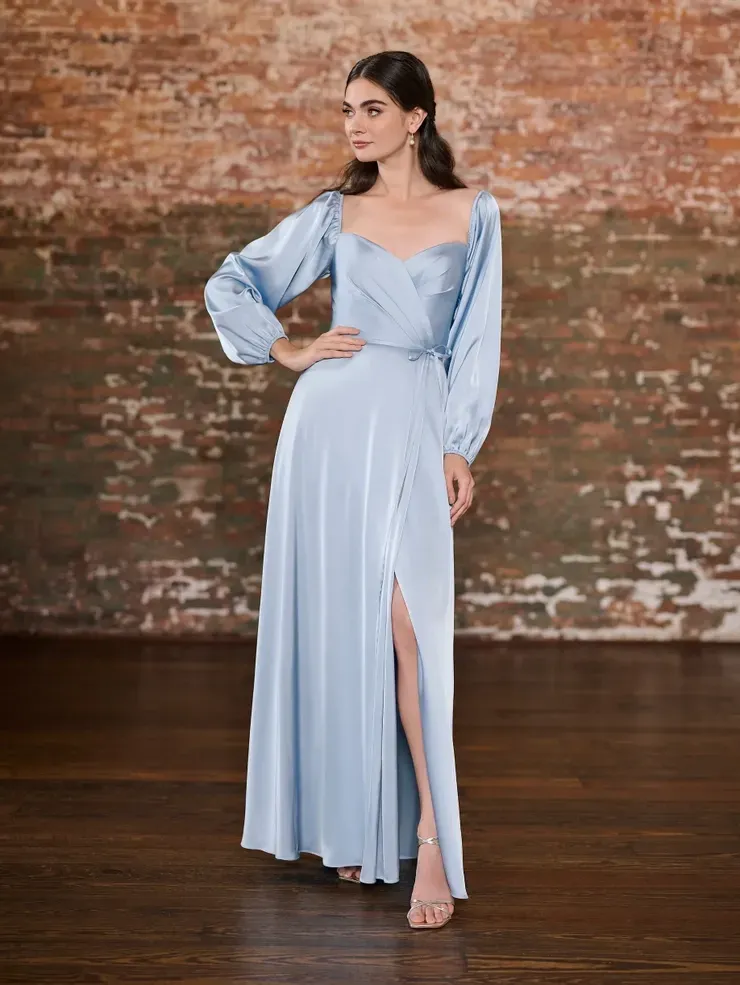 A woman is wearing a light blue satin dress with long sleeves and a high slit.