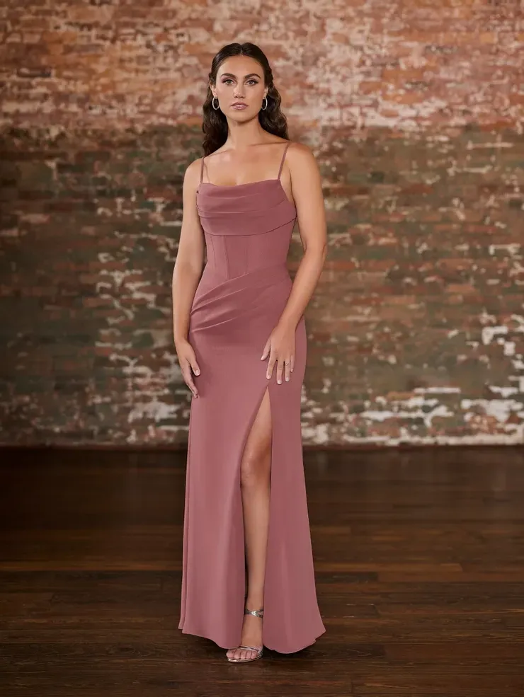A woman in a long pink dress is standing in front of a brick wall.