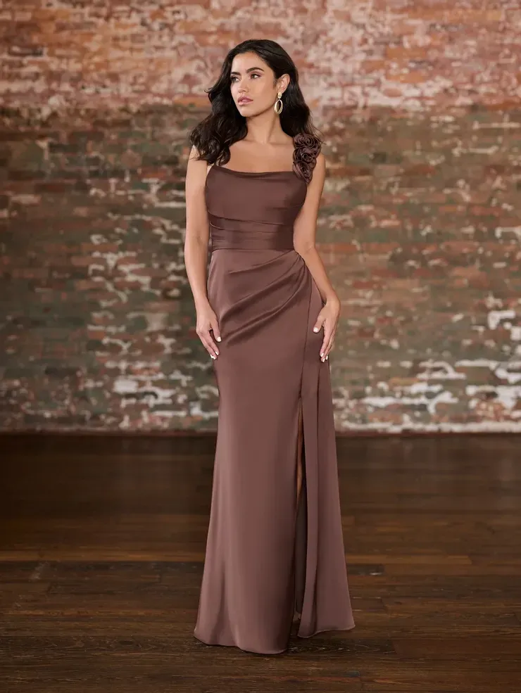 A woman in a long brown dress is standing in front of a brick wall.