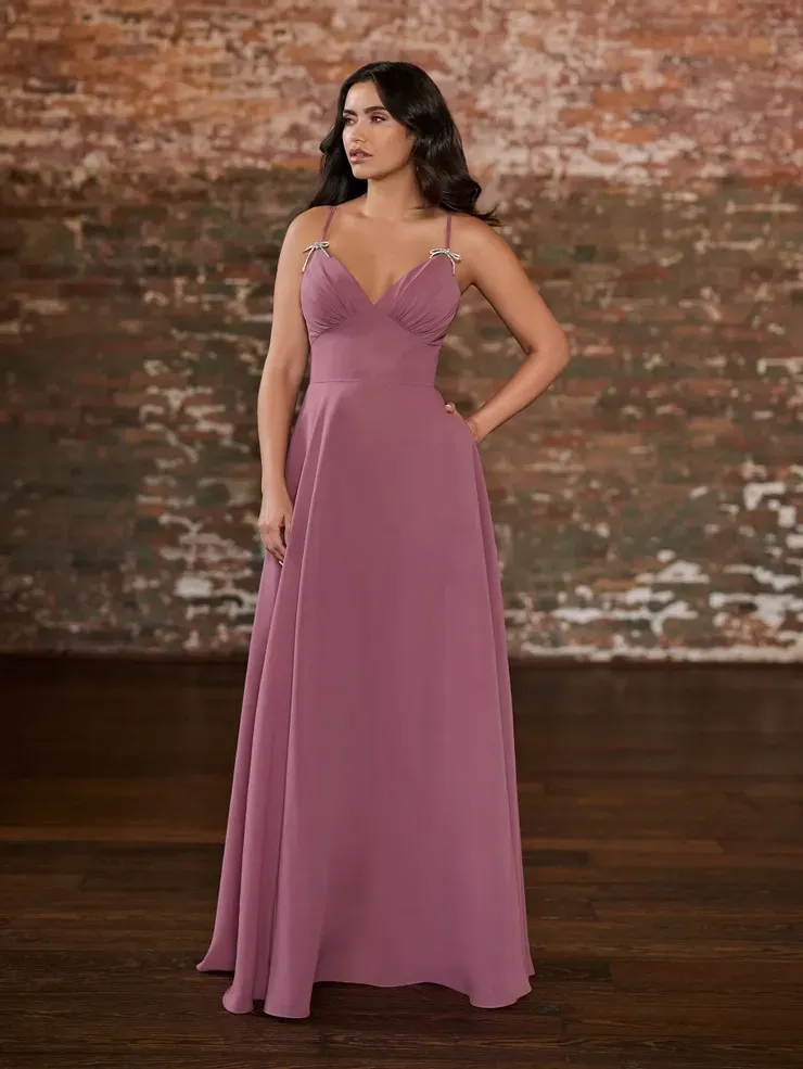 A woman in a long pink dress is standing in front of a brick wall.