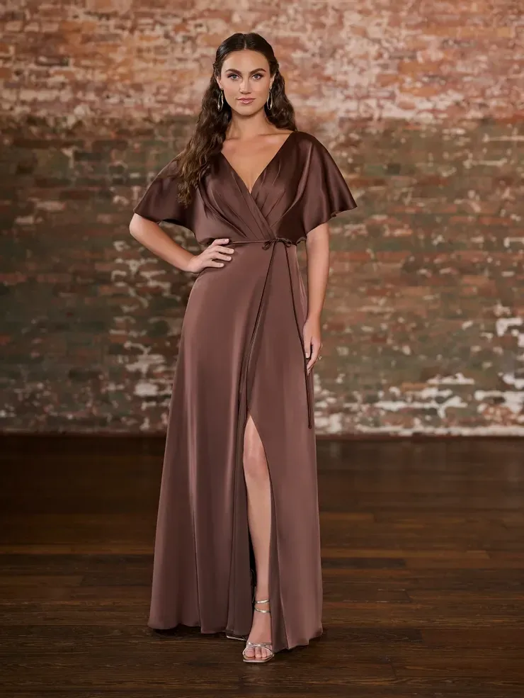 A woman is wearing a brown bridesmaid dress in front of a brick wall.
