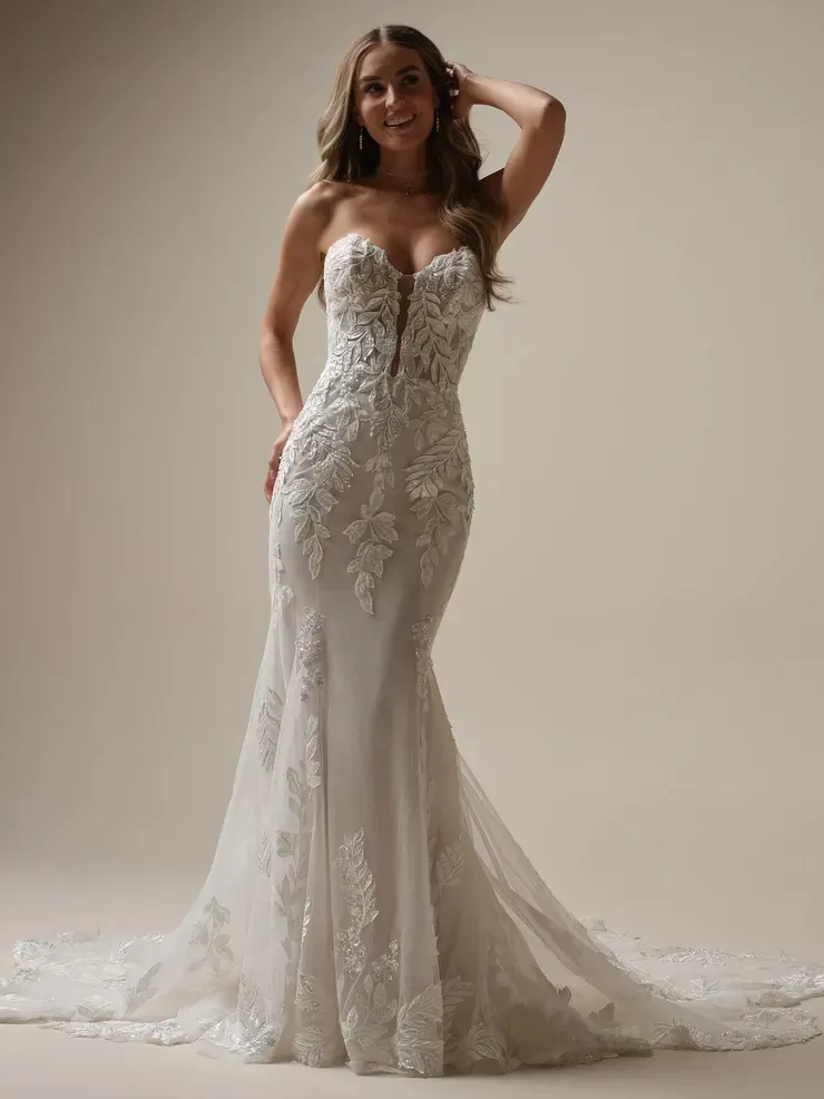 A woman in a white wedding dress is standing in front of a white wall.