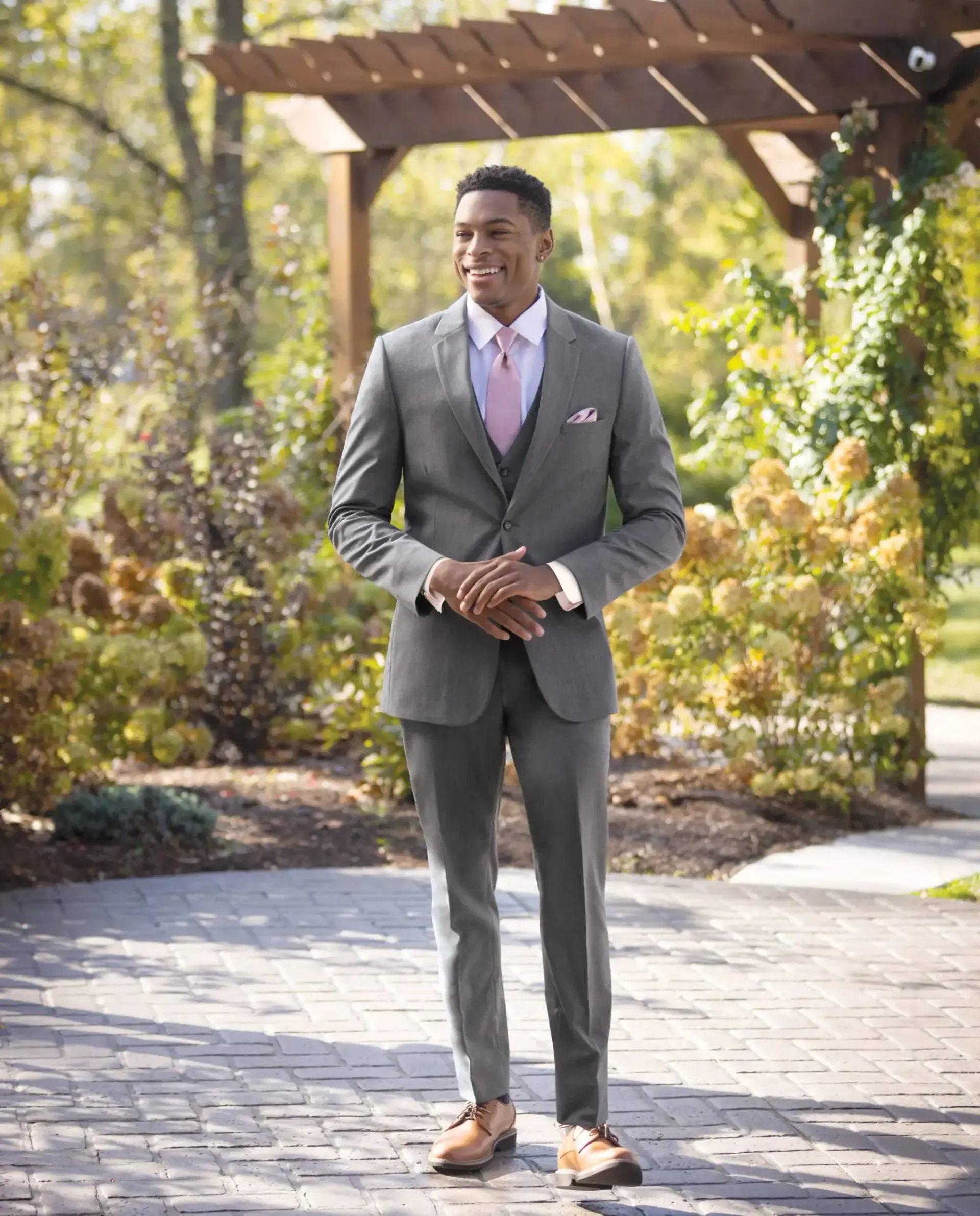 A man in a suit and tie is standing under a pergola.