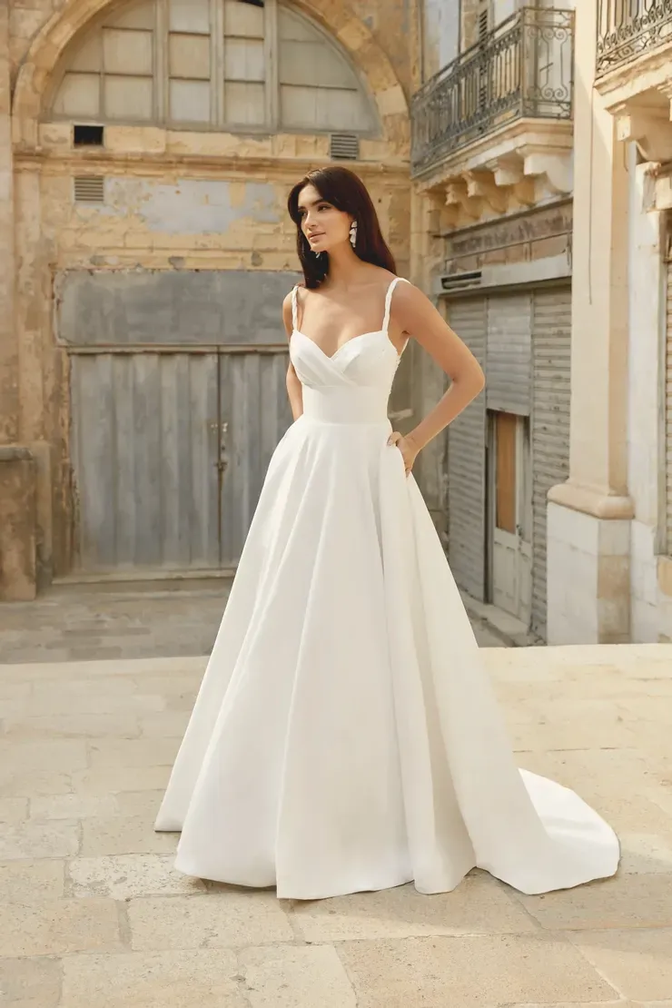 A woman in a white wedding dress is standing in front of a building.