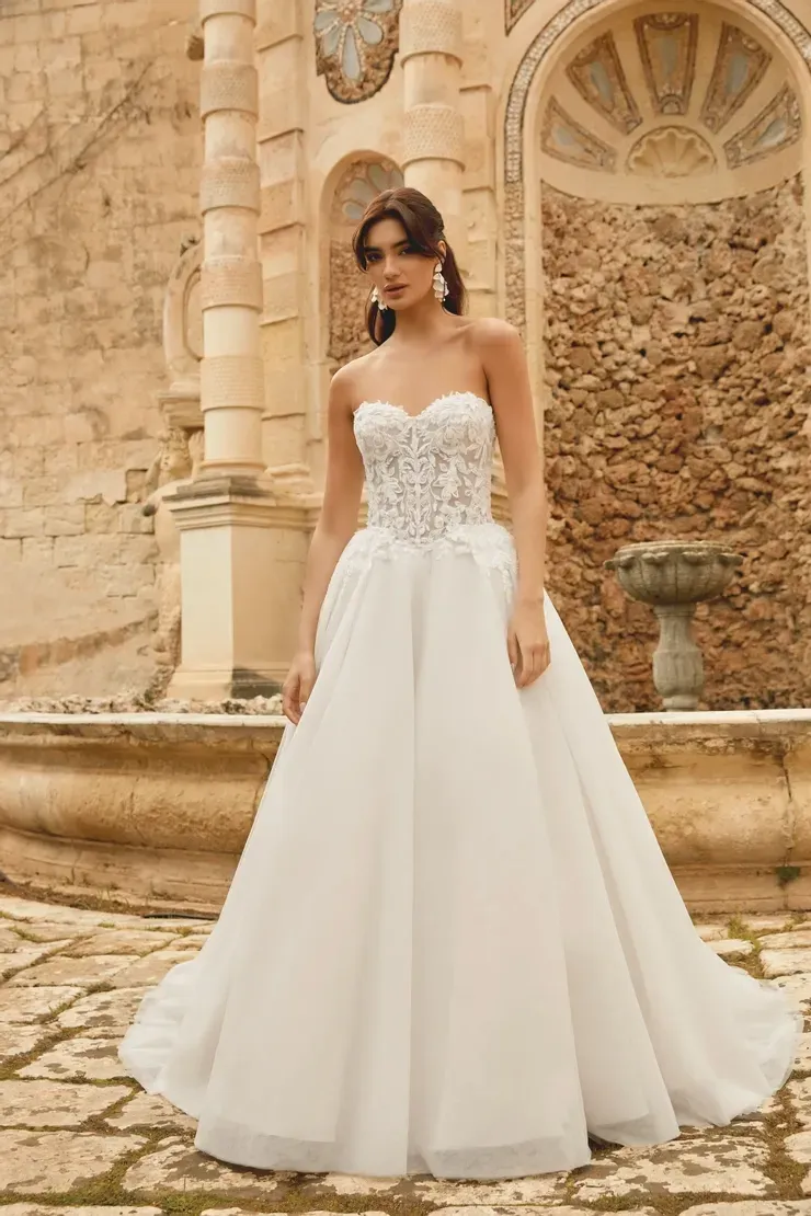 A woman in a white wedding dress is standing in front of a stone wall.
