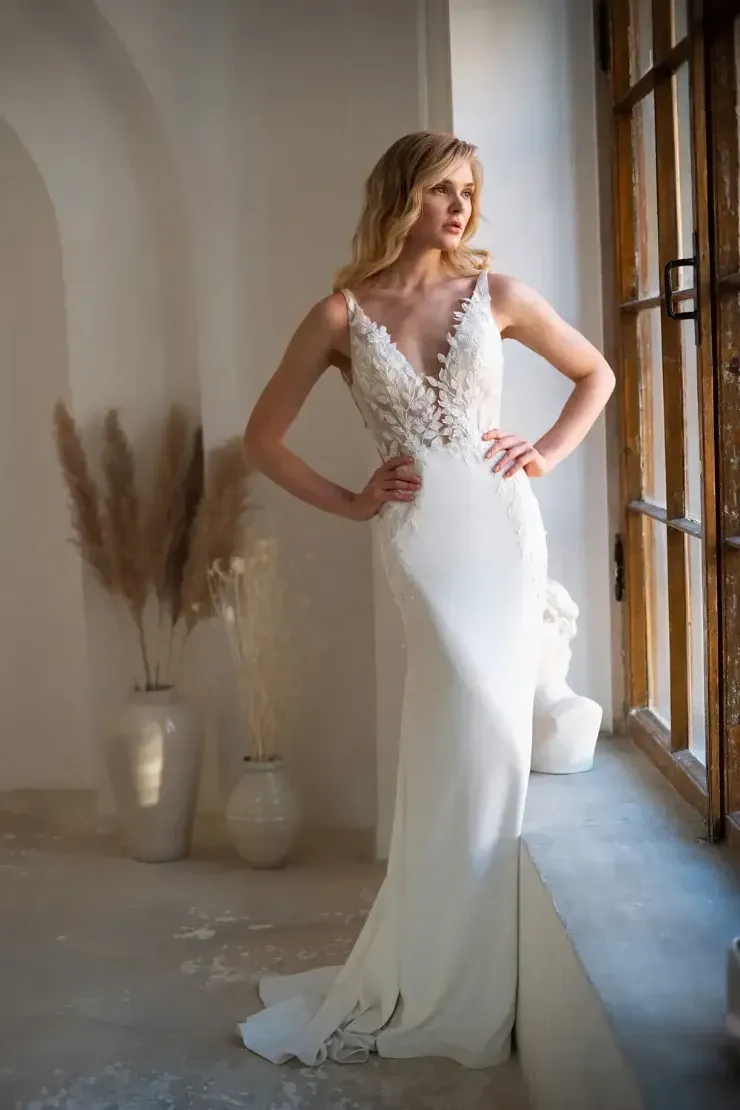 A woman in a white wedding dress is standing in front of a window.