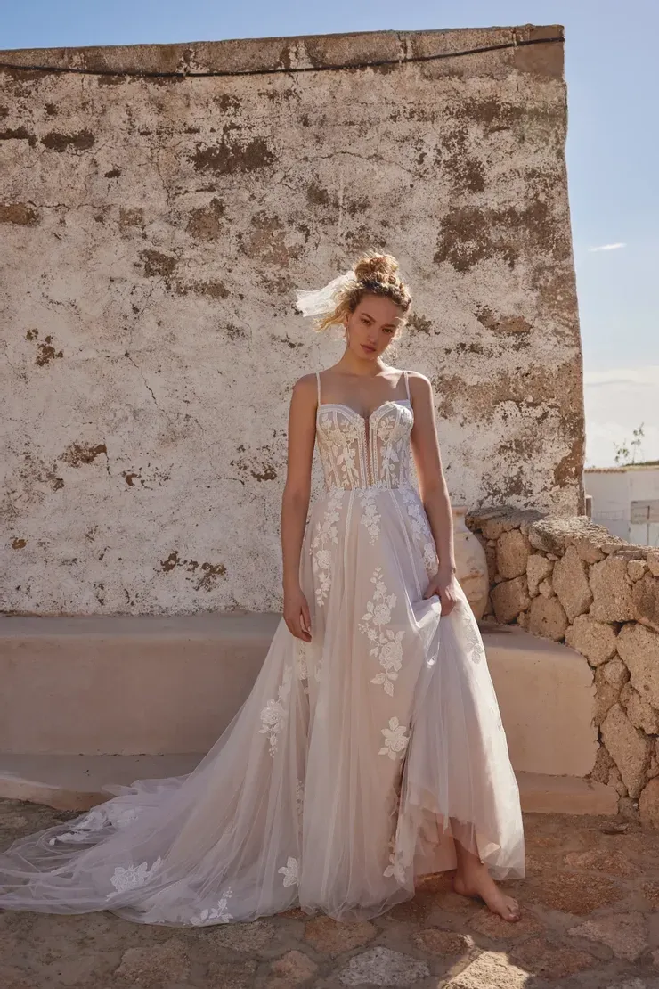 A woman in a wedding dress is standing in front of a stone wall.