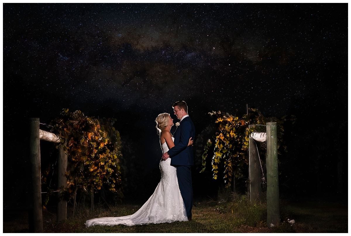 A bride and groom are posing for a picture in a vineyard at night under a starry sky.