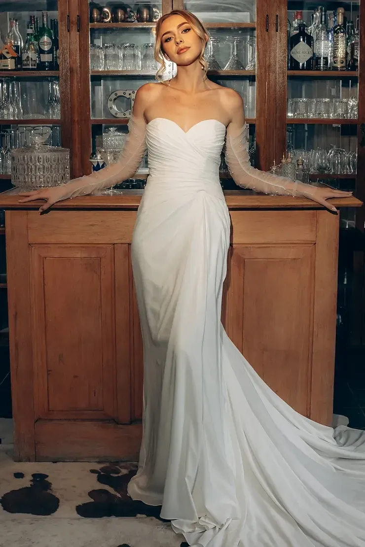 A woman in a white wedding dress is standing in front of a bar.