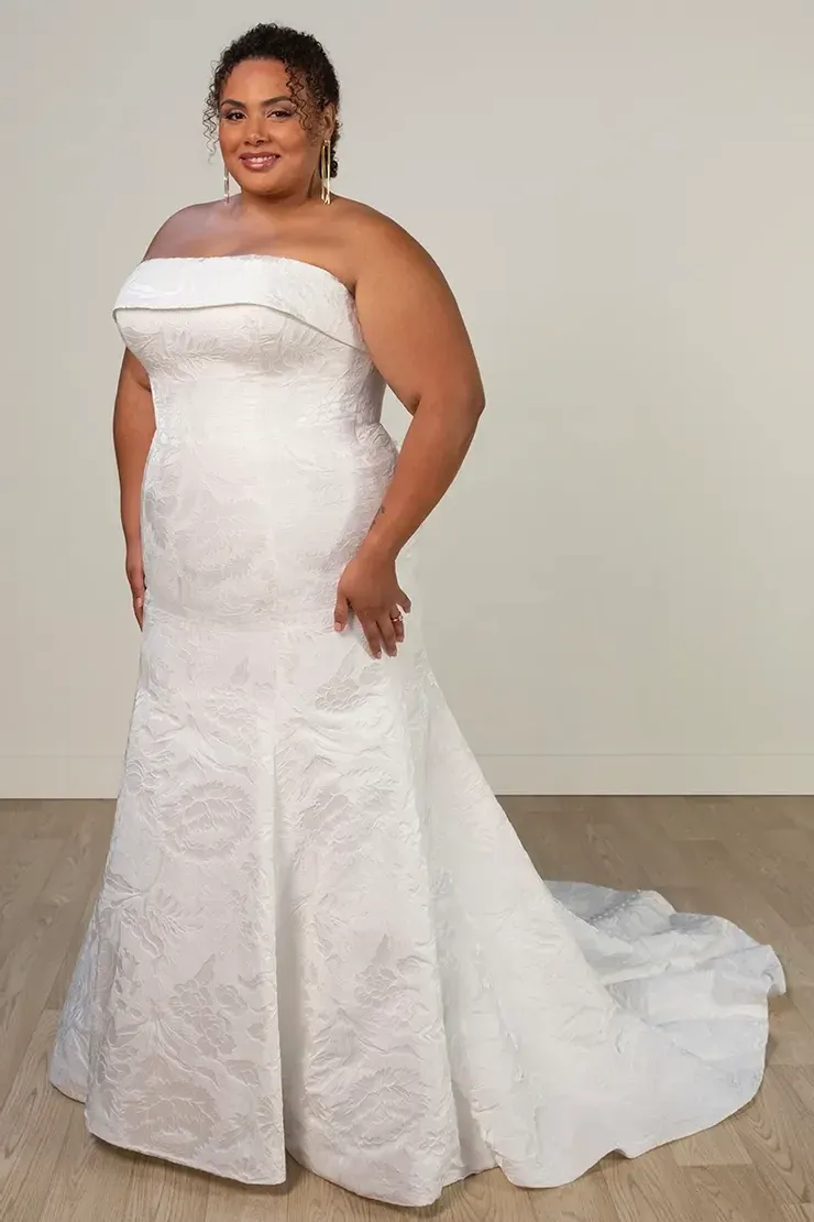A plus size woman is wearing a white strapless wedding dress.