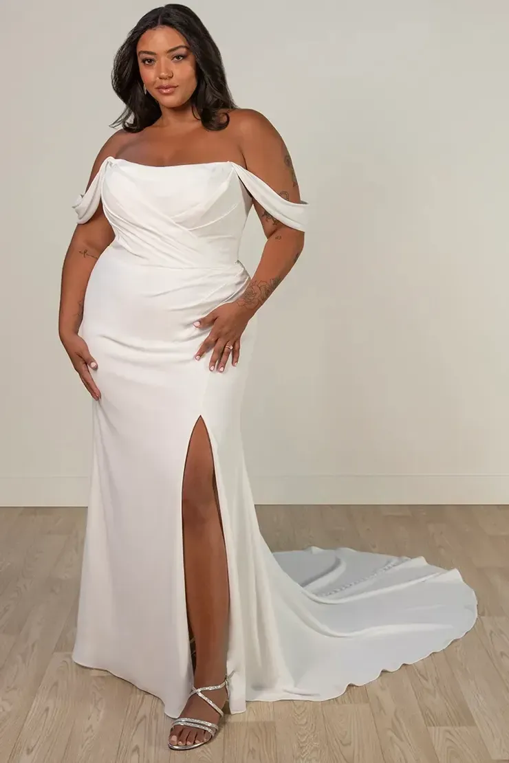 A plus size model is wearing a white wedding dress with a high slit.