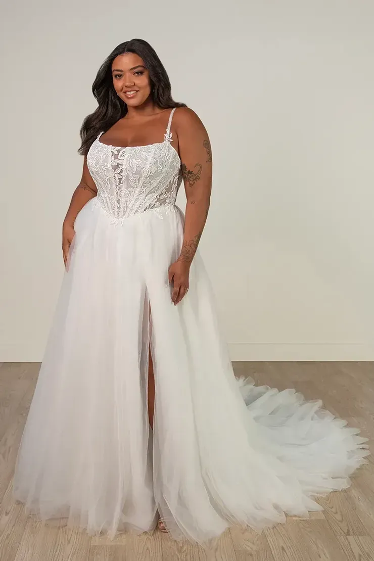 A plus size model is wearing a white wedding dress with a high slit.