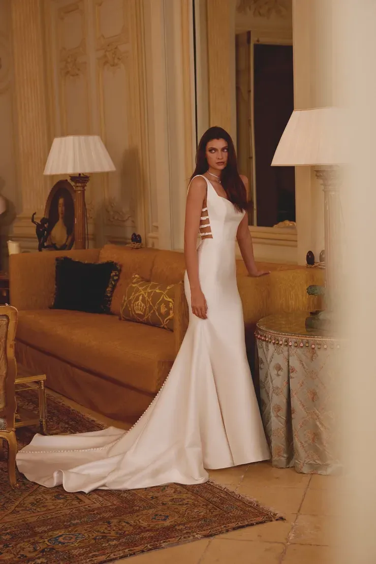 A woman in a white wedding dress is standing in a living room next to a couch.