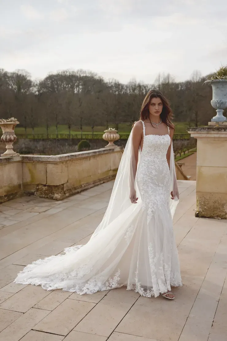 A woman in a white wedding dress and veil is standing on a sidewalk.