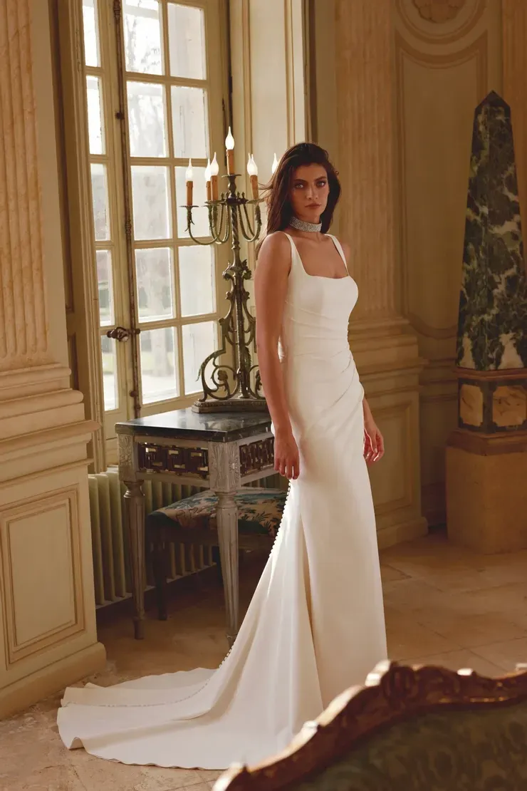 A woman in a white wedding dress is standing in front of a window.