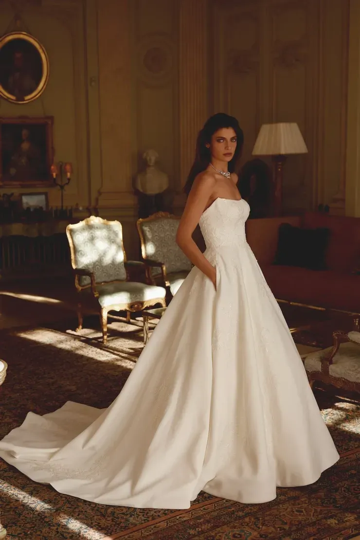 A woman in a white wedding dress is standing in a living room.