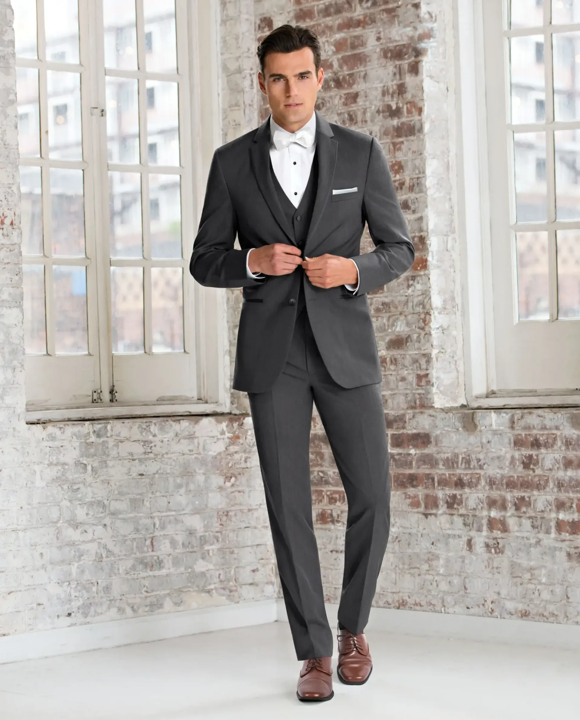 A man in a suit and bow tie is standing in front of a window.