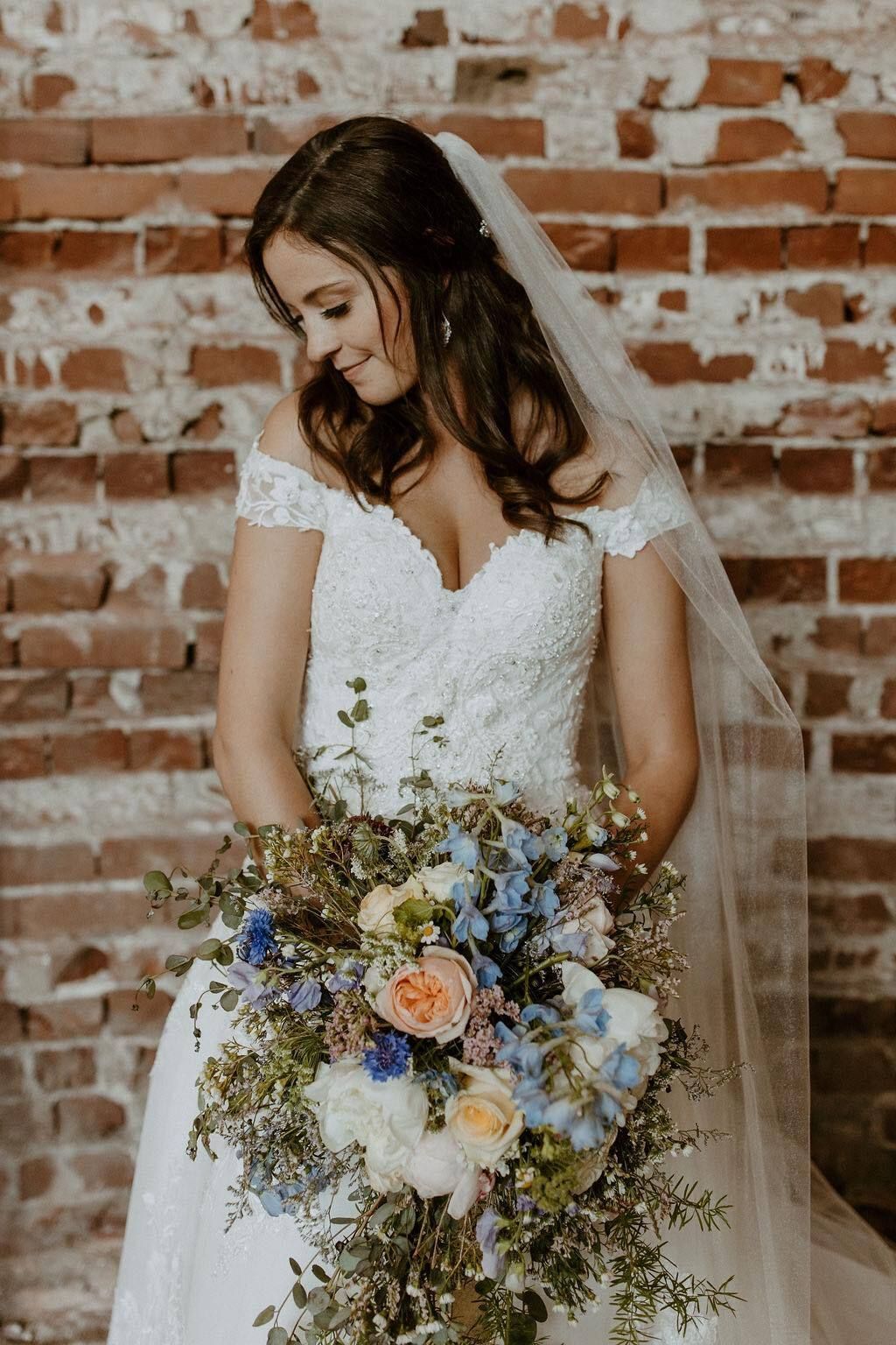 A bride in a wedding dress is holding a bouquet of flowers in front of a brick wall.