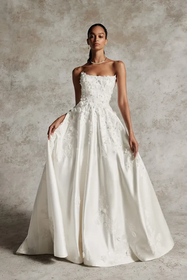A woman in a white wedding dress is standing in front of a wall.