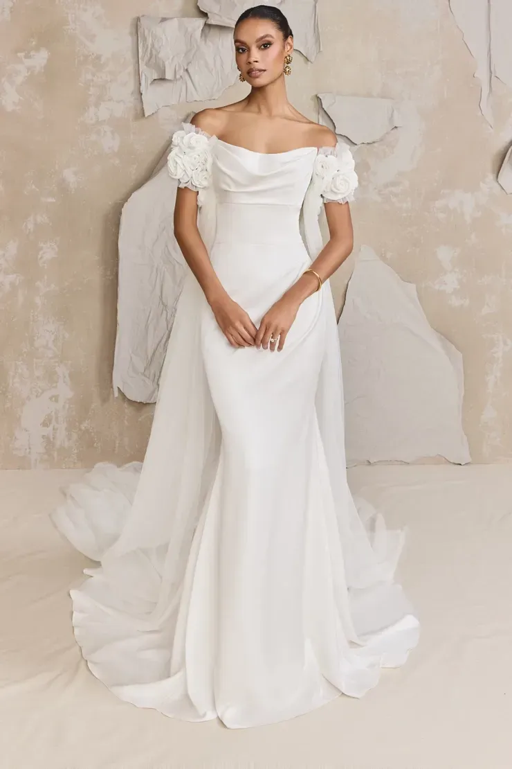 A woman in a white wedding dress is standing in front of a wall.