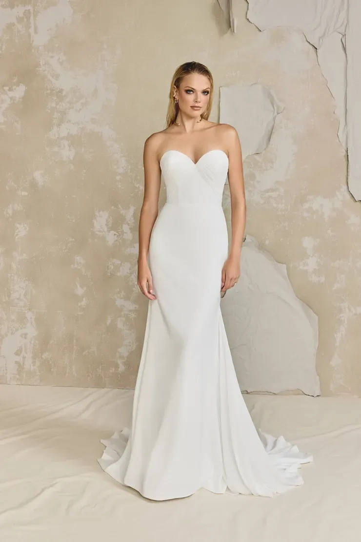 A woman in a white wedding dress is standing in front of a wall.