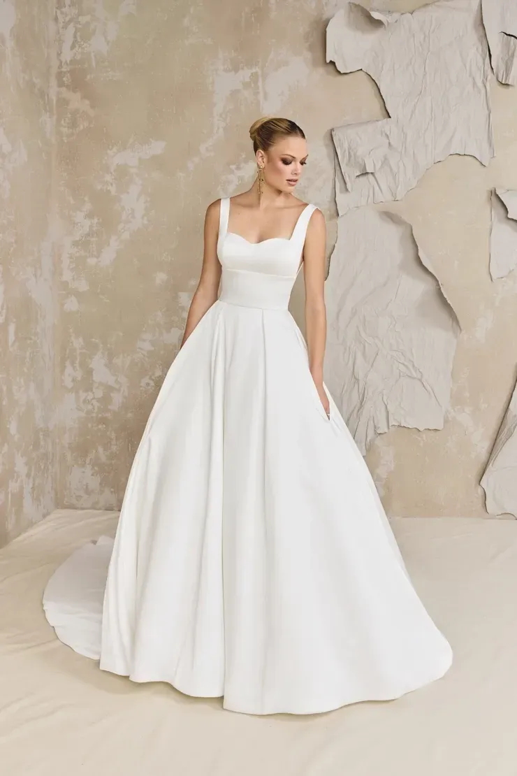 A woman in a white wedding dress is standing in front of a wall.