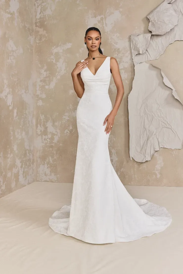 A woman in a white wedding dress is standing in front of a wall.
