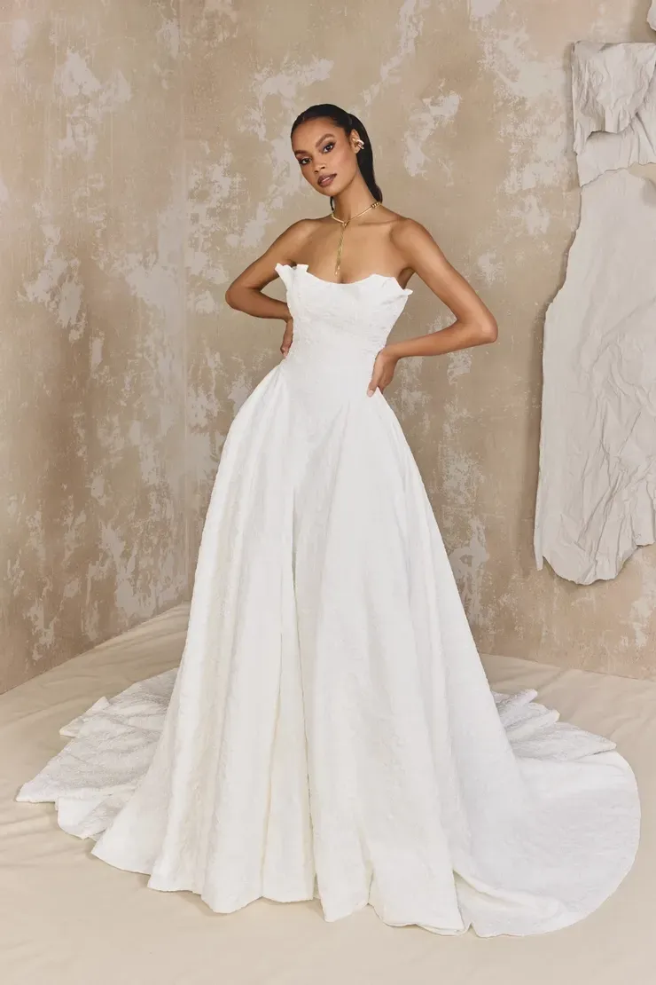 A woman in a white wedding dress is standing in front of a wall.