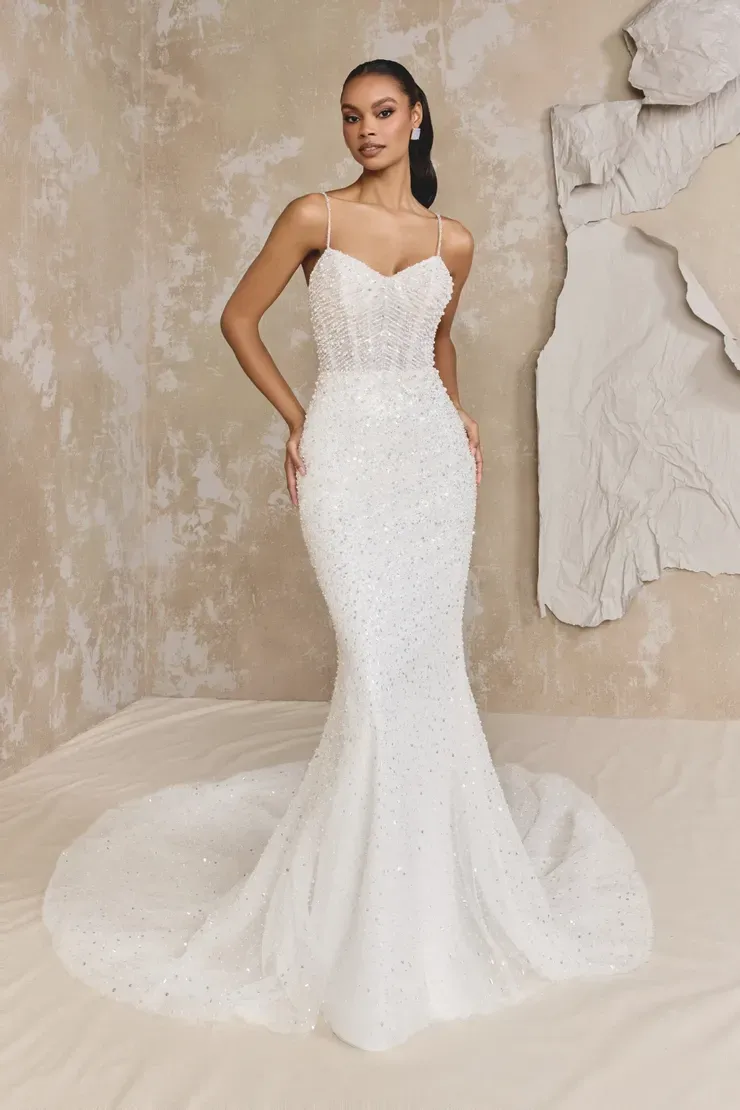 A woman in a white wedding dress is standing in front of a wall.