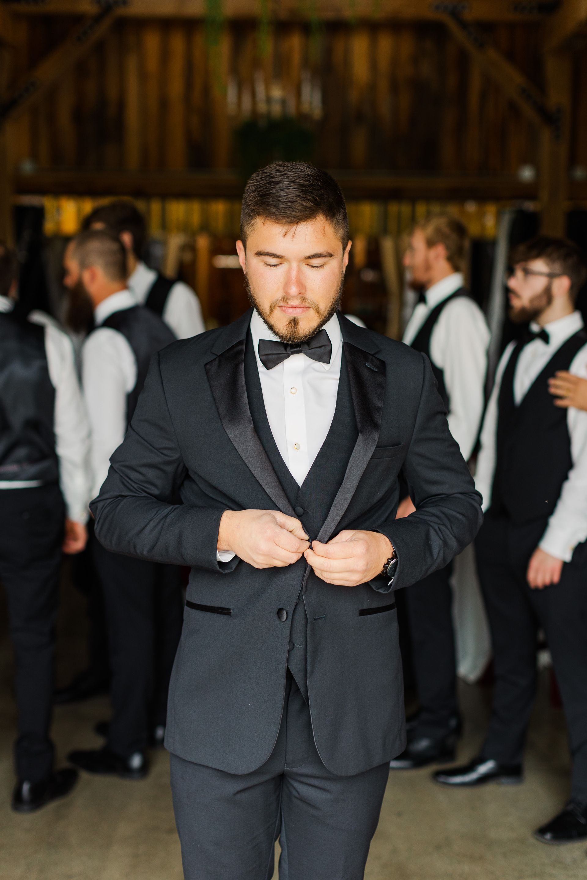 A man in a tuxedo and bow tie is standing in front of his groomsmen.