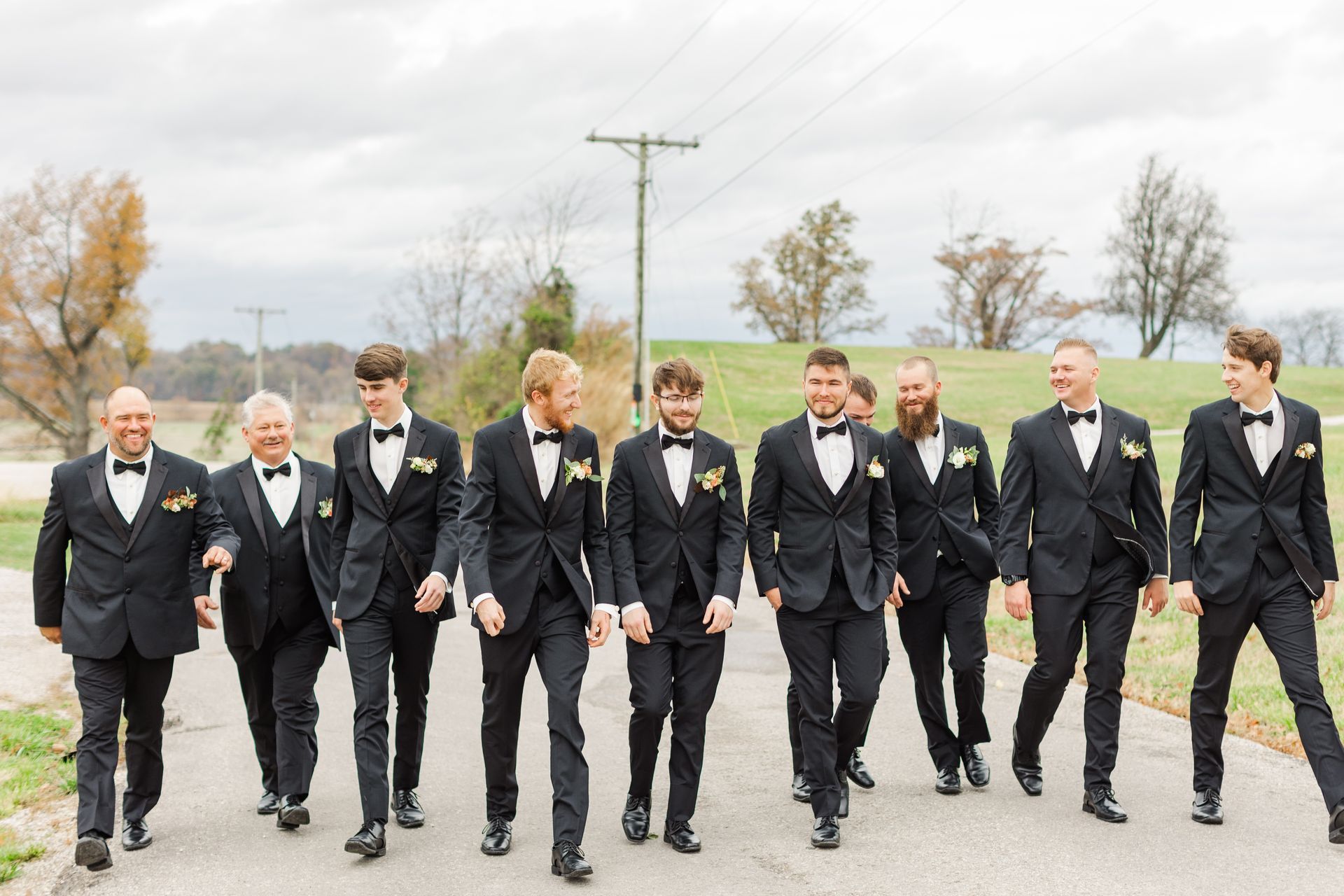 A group of men in tuxedos and bow ties are walking down a road.