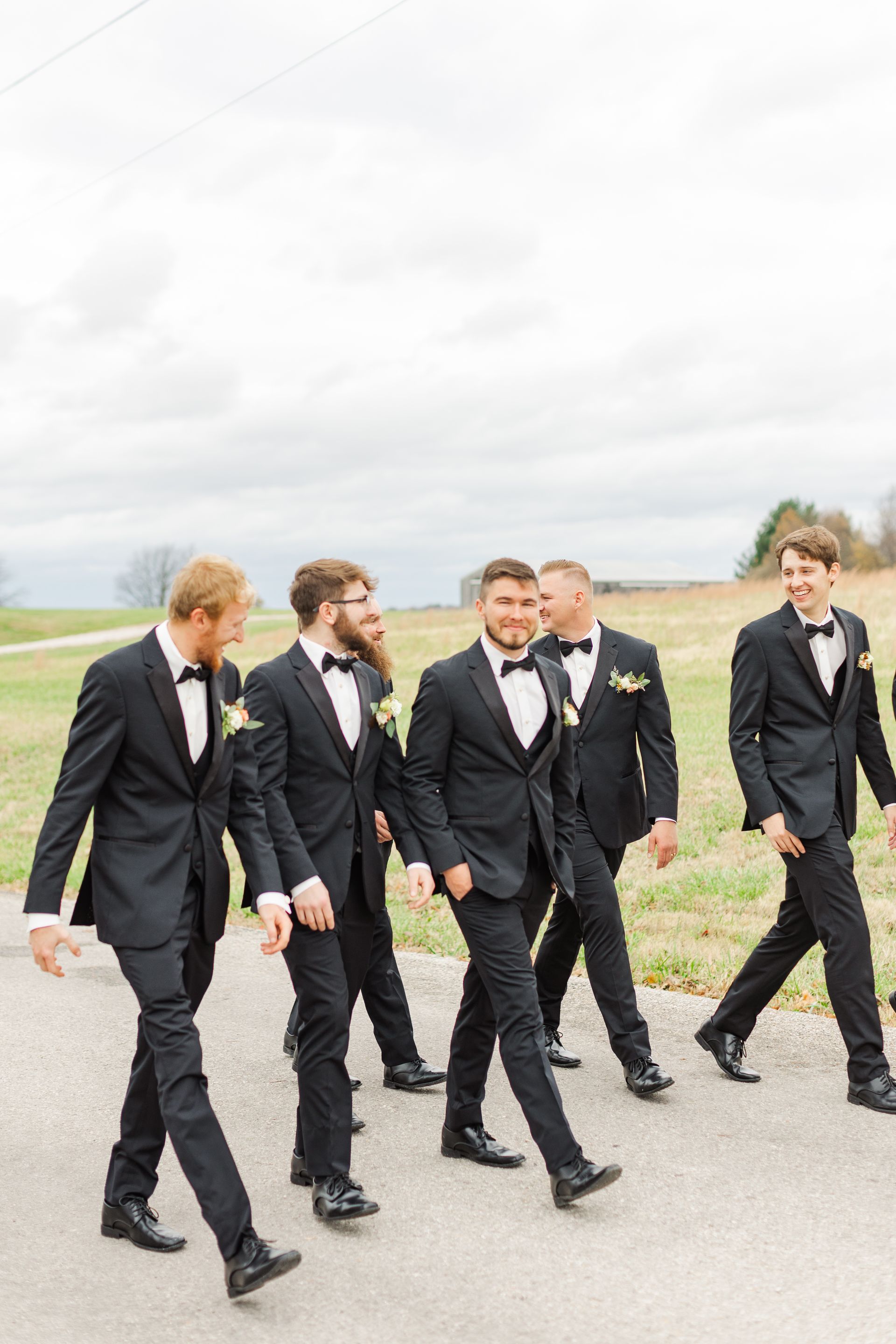 A group of men in tuxedos and bow ties are walking down a road.