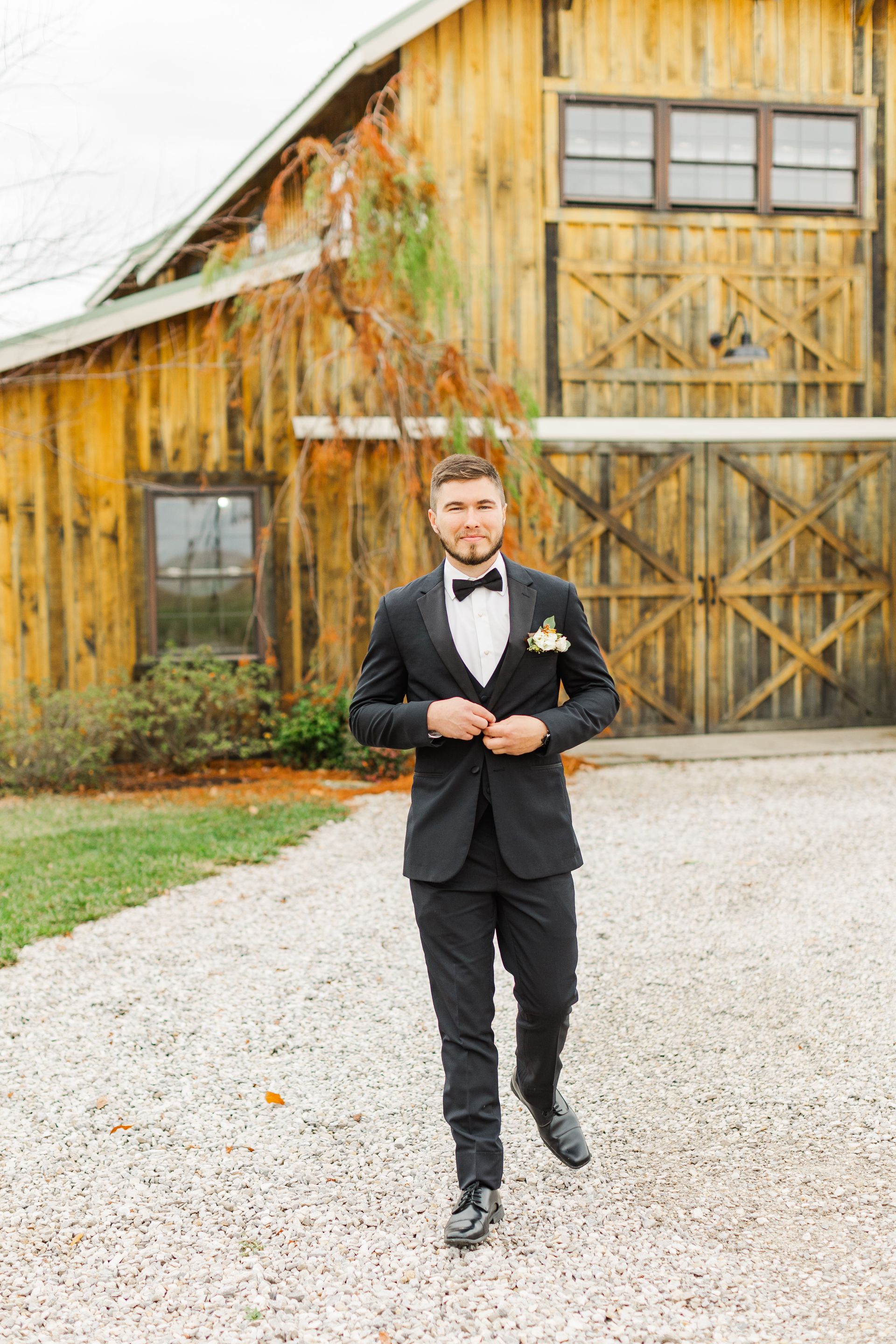 A man in a tuxedo and bow tie is standing in front of a wooden building.