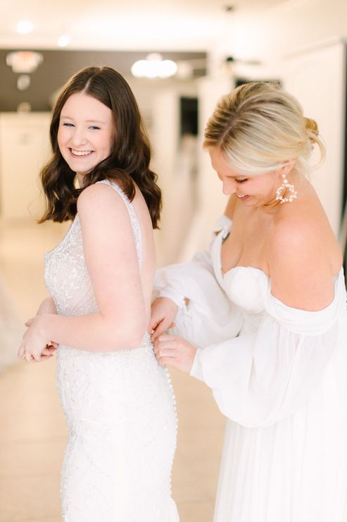 A woman is helping another woman put on her wedding dress.