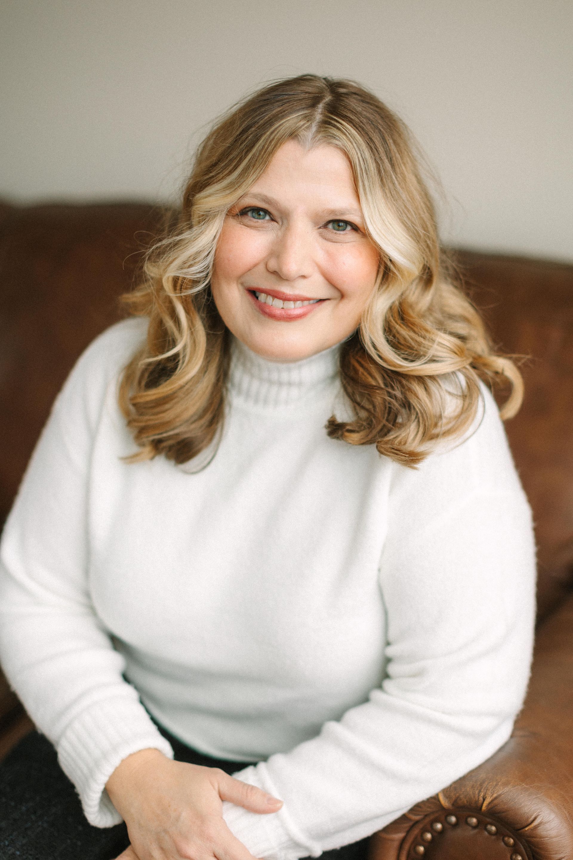 A woman in a white shirt is sitting on a brown couch.