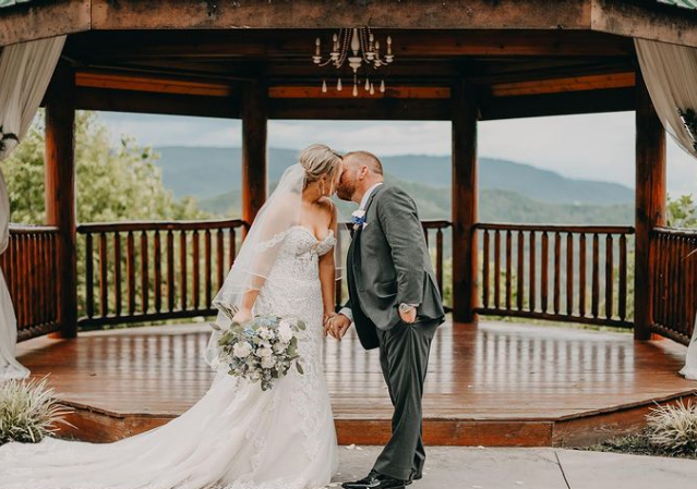 A bride and groom are kissing in front of a gazebo.