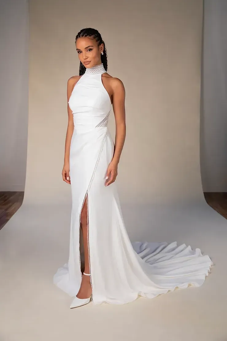 A woman in a white wedding dress is standing in front of a white wall.