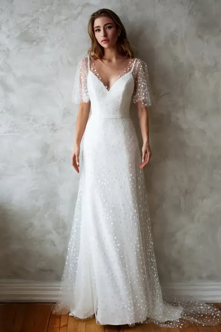 A woman in a white wedding dress is standing in front of a wall.