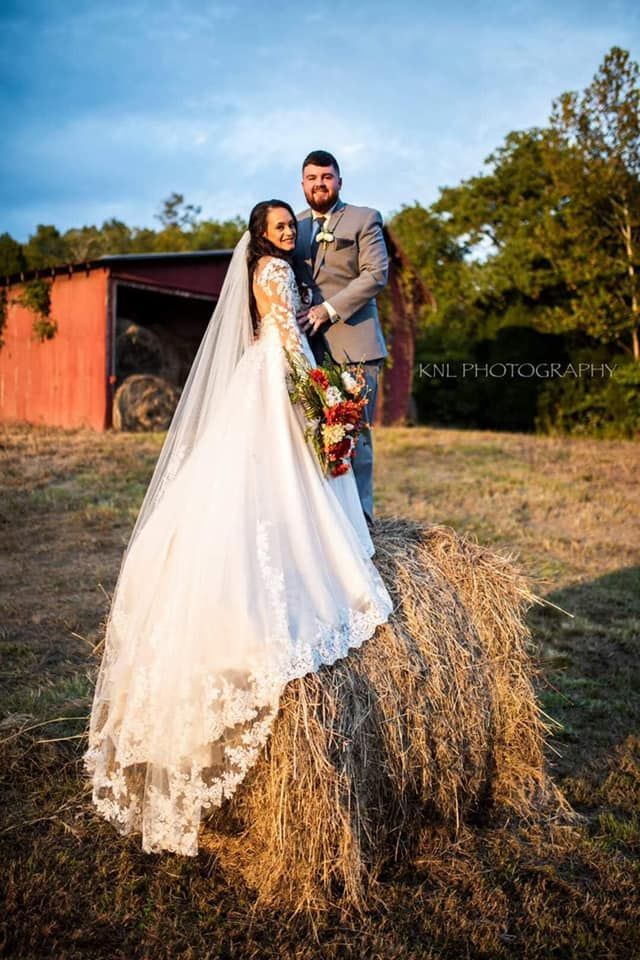 A bride and groom are standing on top of a bale of hay.